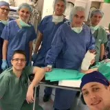 Zespół chirurgów w strojach operacyjnych pozuje do zdjęcia w sali operacyjnej, jeden z nich trzyma nogę w gipsie.
