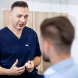 Dentysta w granatowym uniformie pokazuje pacjentowi model szczęki.