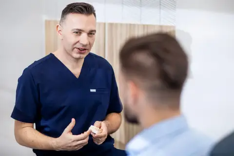 Dentysta w granatowym uniformie pokazuje pacjentowi model szczęki.