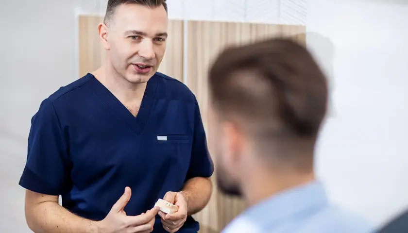 Dentysta w granatowym uniformie pokazuje pacjentowi model szczęki.