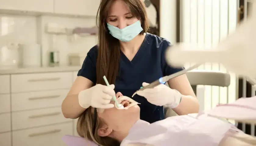 Dentystka w masce i rękawiczkach wykonuje zabieg u pacjentki w gabinecie stomatologicznym.